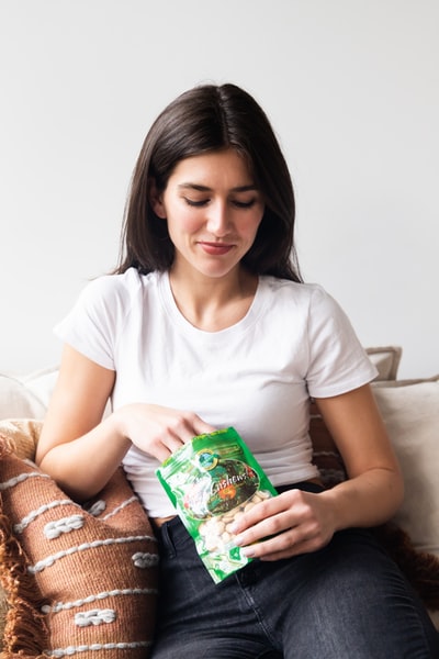 ソファーに座った白いTシャツを着ている女性がナッツを食べようとしている画像